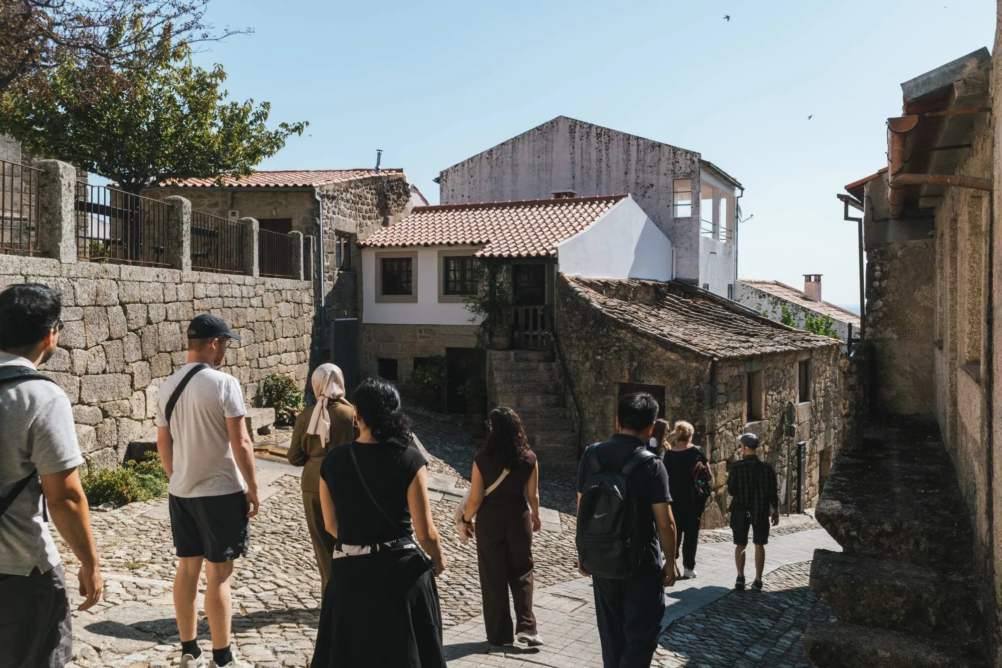 The group walks down a cobbled lane between granite houses in Castelo Novo.