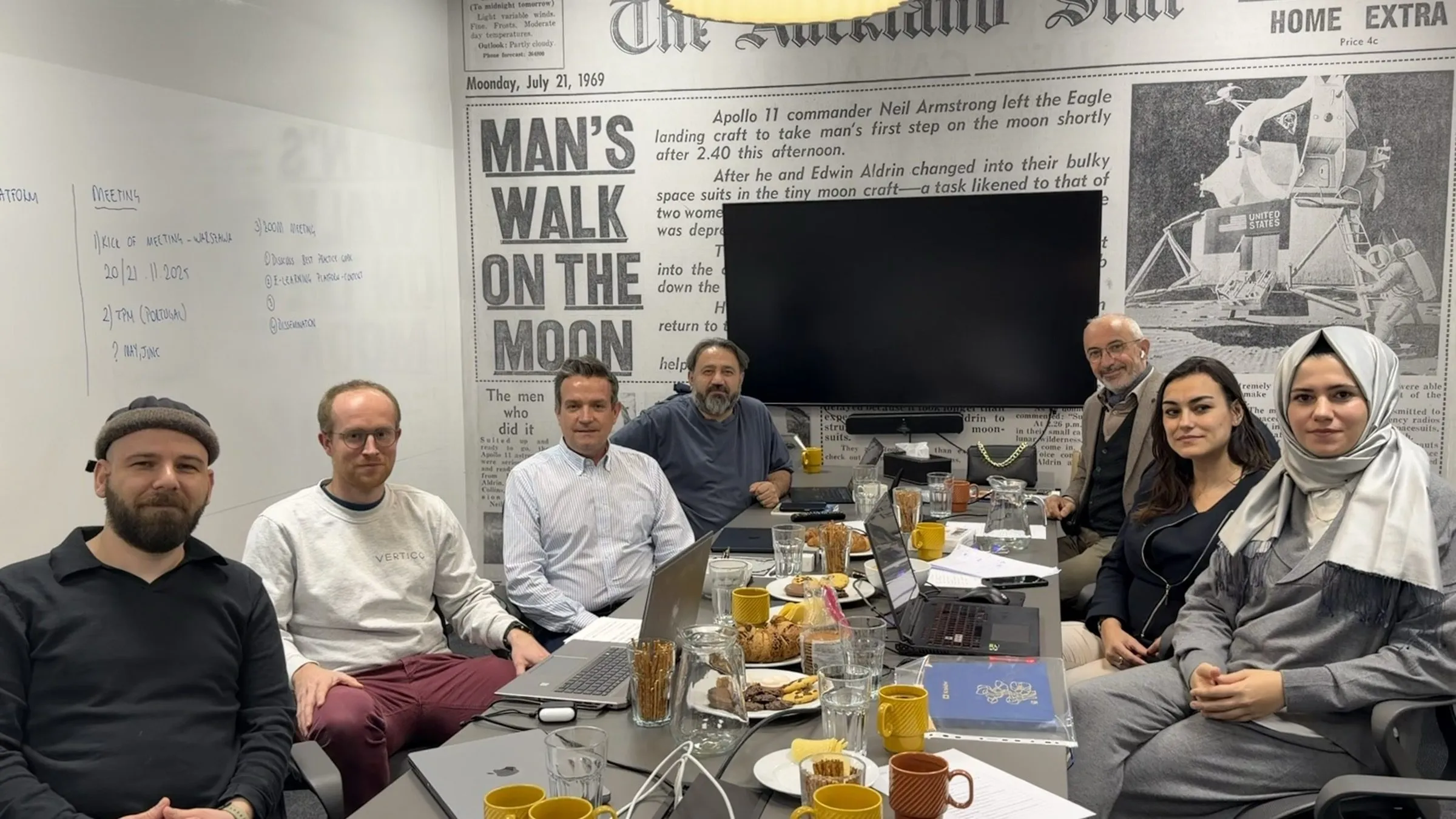 Members of the partner teams seated around the meeting table in Warsaw, smiling at the camera.