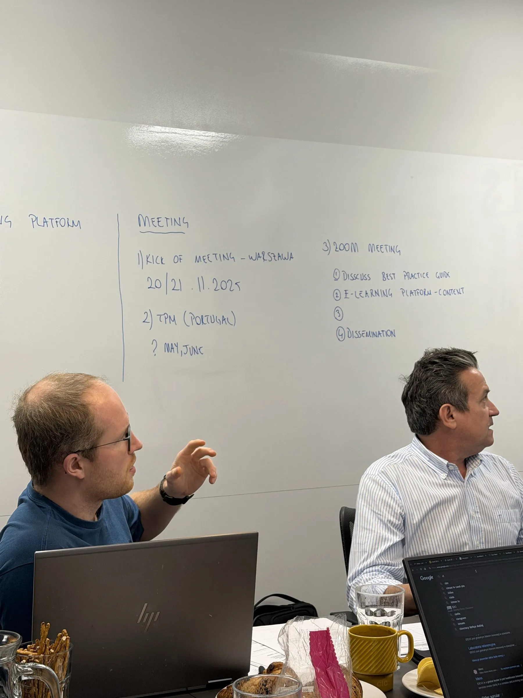 Two partners at the table in front of a whiteboard listing the meetings ahead: the kick-off in Warsaw on 20 and 21 November 2025, a partner meeting in Portugal, and an online meeting on the guide, the e-learning platform and dissemination.