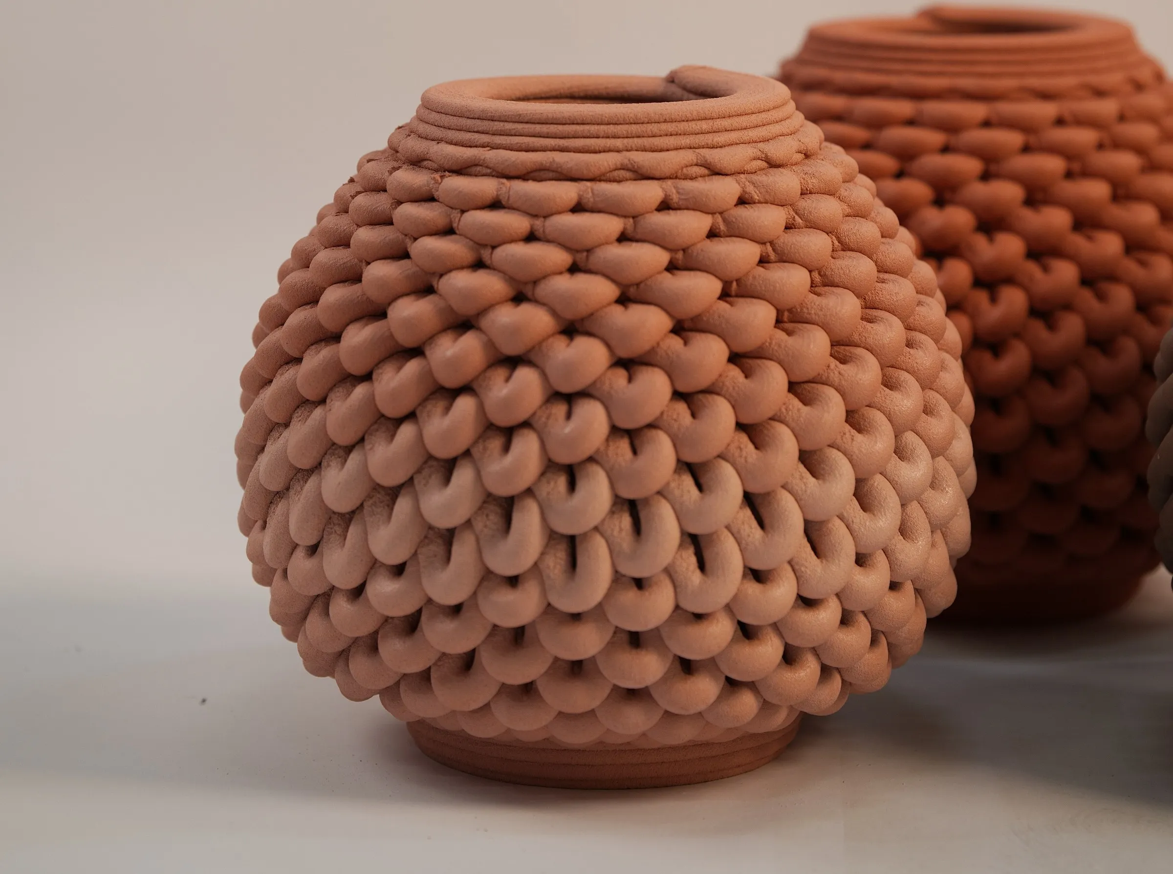 Vessels 3D printed from raw earth, their surface built from looped beads of clay.